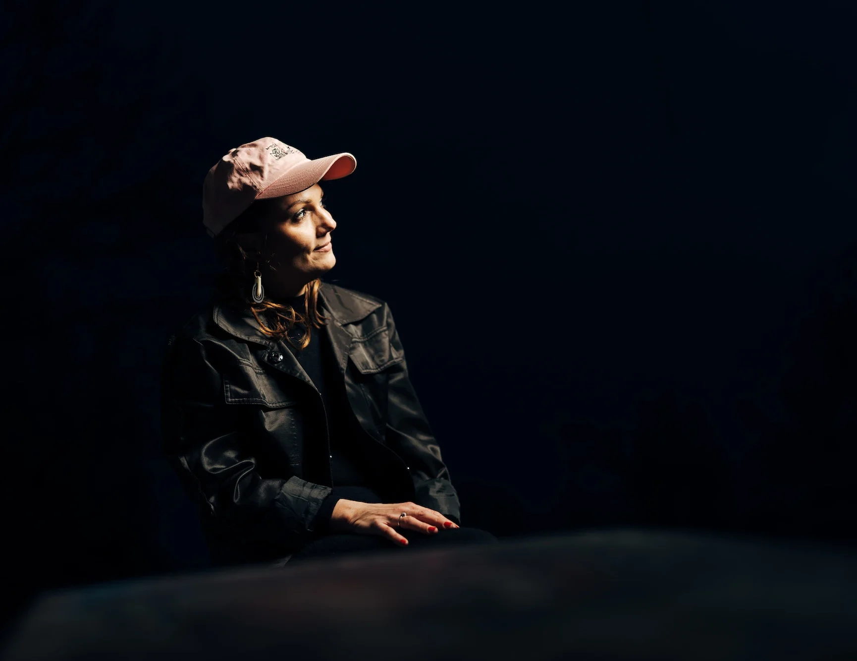 Rosanna Grüter trägt ein rosa Cap und schwarze Jacke, sitzt an einem Tisch und schaut nach rechts in die Ferne.