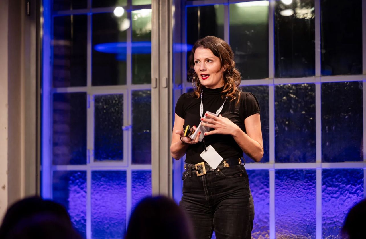 Rosanna Grüter spricht vor einem Publikum in einem blau weiss beleuchteten Saal.