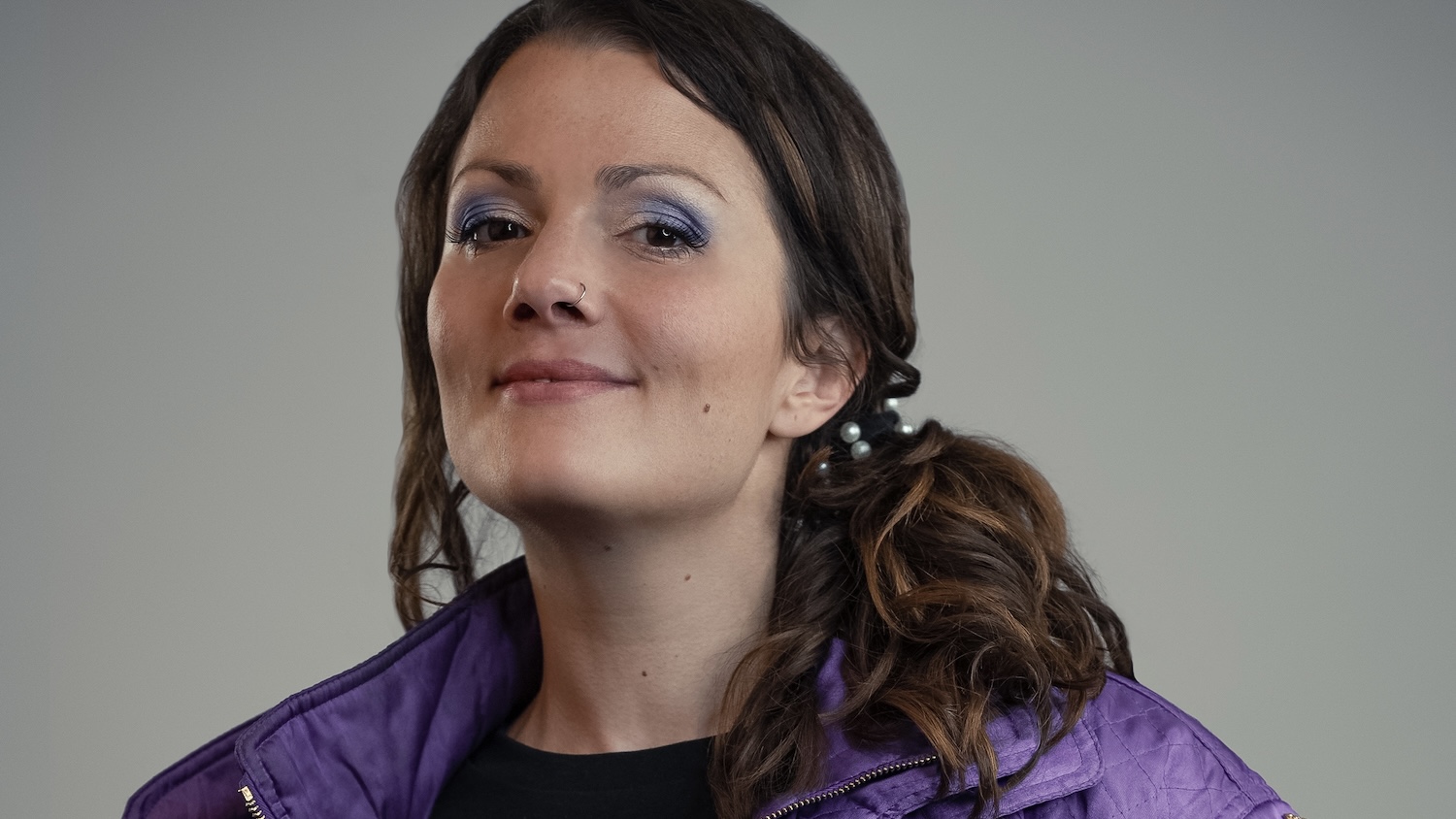 Portrait von Rosanna Grüter welche vor einem grauen hintergrund in die Kamera lacht.